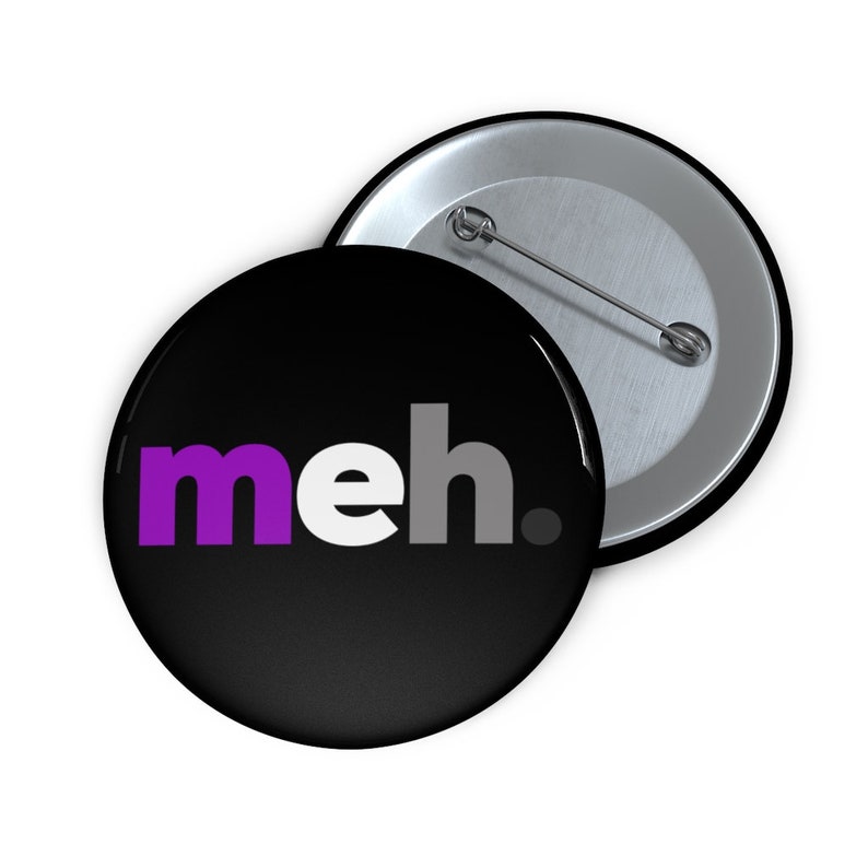 May include: A black button with a white background and the word "meh." in purple, white, and gray letters. The button has a silver back.