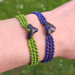 May include: Two bracelets with hand-carved black stone charms. One bracelet is green and the other is blue. The bracelets are on a person's wrist. The text "Gaia Hand Carved ELEGANTLY WILD!" is visible in the image.