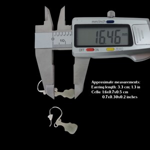May include: A pair of jade green earrings shaped like a cello, measured with a digital caliper showing 16.46 mm. The earrings are 3.3 cm or 1.3 inches long. The cello is 1.6 cm by 0.7 cm by 0.5 cm or 0.7 inches by 0.3 inches by 0.2 inches.