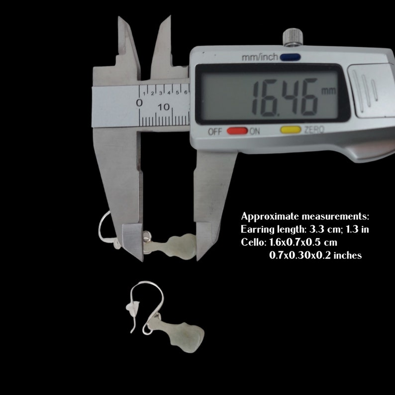 May include: A pair of jade green earrings shaped like a cello, measured with a digital caliper showing 16.46 mm. The earrings are 3.3 cm or 1.3 inches long. The cello is 1.6 cm by 0.7 cm by 0.5 cm or 0.7 inches by 0.3 inches by 0.2 inches.