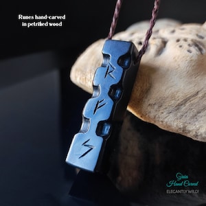 Può includere: Collana con ciondolo nero con tre rune intagliate. Il ciondolo è in legno pietrificato ed è intagliato a mano. La collana è su un cordoncino marrone.