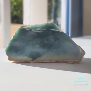 Könnte beinhalten: Ein großes, unregelmäßig geformtes Stück grüner Jade mit einem hellgrünen und weißen Marmormuster. Der Jade ist glatt und poliert.