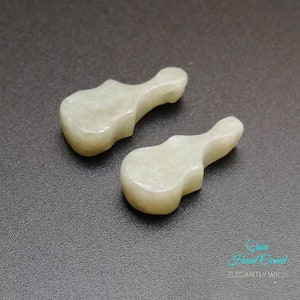 May include: Two hand-carved white jade guitar pendants. The pendants are smooth and polished, with a slightly translucent appearance.