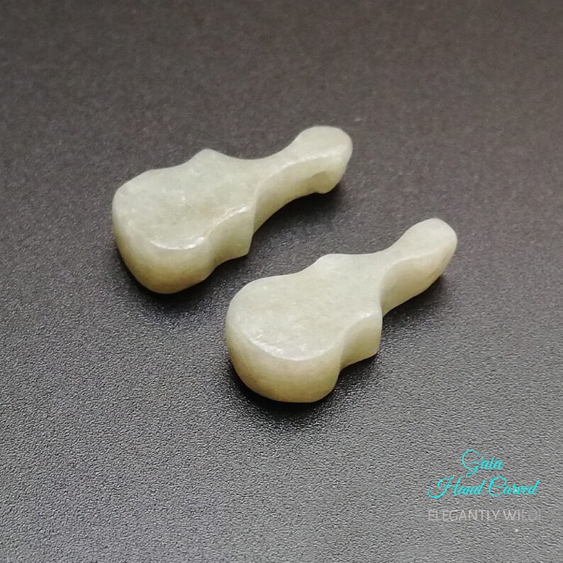 May include: Two hand-carved white jade guitar pendants. The pendants are smooth and polished, with a slightly translucent appearance.