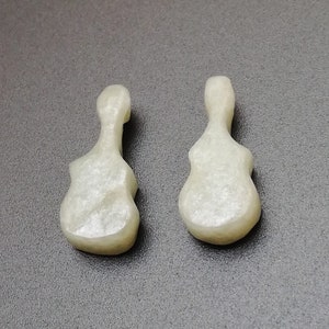 May include: Two white, ceramic guitar-shaped pendants. The pendants have a smooth, slightly textured surface.