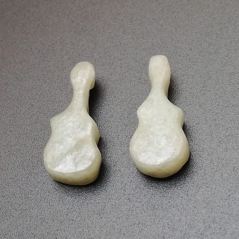 May include: Two white, ceramic guitar-shaped pendants. The pendants have a smooth, slightly textured surface.