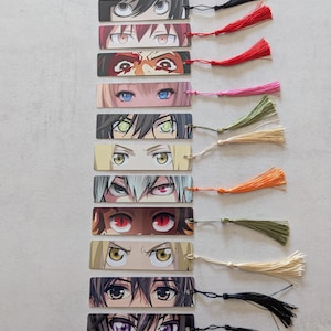 Può includere: Una collezione di segnalibri in stile anime, ognuno con diversi disegni di occhi. Ogni segnalibro ha un colore e uno stile di occhi diverso, con nappe nere. I segnalibri rettangolari sono disposti verticalmente, mostrando una varietà di occhi di personaggi anime.