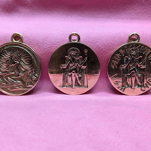 Puede incluir: Tres colgantes de metal de color dorado con diferentes diseños. El primer colgante presenta a una mujer con el pelo suelto montando un delfín. El segundo colgante presenta a una mujer sentada en un trono con un cetro. El tercer colgante presenta a una mujer sentada en un trono con un cetro y las palabras "SUMMA VERITAS" alrededor del borde.