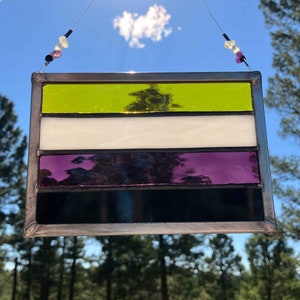 May include: A stained glass window depicting the non-binary pride flag. The flag has five horizontal stripes: yellow, white, purple, black, and a final yellow stripe.