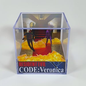 Op de afbeelding: Een transparante kubusvormige displaycase van plastic met een diorama erin. Het diorama toont een scène uit de videogame Resident Evil: Code Veronica. De scène toont twee personages, een man en een vrouw, die door een gang lopen met vlammen op de vloer. De tekst "RESIDENT EVIL CODE: Veronica" is gedrukt op de basis van de kubus.