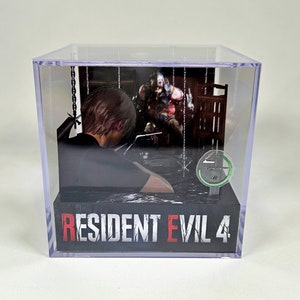 May include: A clear plastic cube display case with a 3D diorama of a character from the video game Resident Evil 4. The diorama features a character in a dark shirt and a zombie-like figure in the background. The text "RESIDENT EVIL 4" is printed on the base of the display case.