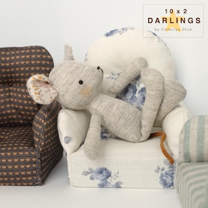 May include: A grey stuffed mouse doll resting on a miniature armchair with a floral pattern. The doll has a light brown tail and a patterned ear. The armchair is white with blue floral designs. The text "10 x 2 Darlings by Viktoriya Zhuk" is in the upper right corner.