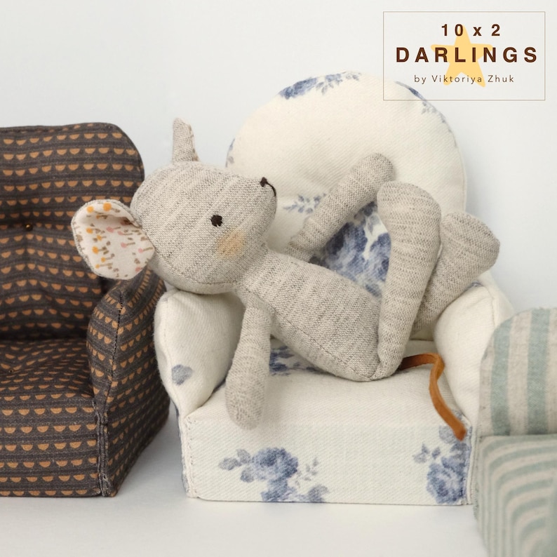 May include: A grey stuffed mouse doll resting on a miniature armchair with a floral pattern. The doll has a light brown tail and a patterned ear. The armchair is white with blue floral designs. The text "10 x 2 Darlings by Viktoriya Zhuk" is in the upper right corner.