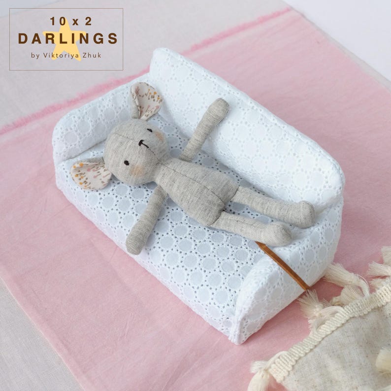 May include: A grey stuffed mouse toy lies on a white, eyelet-detailed miniature couch. The couch is set on a pink surface. The mouse has patterned ears and is lying down. The text "10 x 2 DARLINGS by Viktoriya Zhuk" is in the upper left corner.