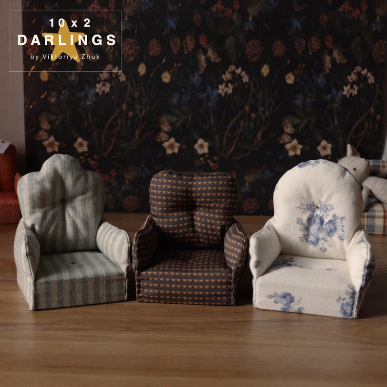 May include: Three miniature armchairs with varied upholstery patterns. The left chair features blue and white stripes, the middle one has a brown and gold pattern, and the right chair has a floral design. A dark floral wallpaper forms the backdrop.