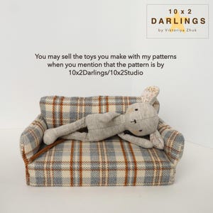 May include: A grey stuffed bunny lies on a miniature sofa with a blue, brown, and cream plaid pattern. The image includes the text "10 x 2 DARLINGS by Viktoriya Zhuk" and a message about selling toys made with the patterns.