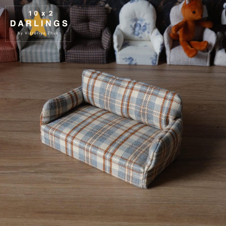 May include: A miniature sofa with a blue, beige, and brown plaid pattern. The small couch has a rectangular shape with a backrest and armrests. The image also shows other miniature chairs in the background. Text on the image reads "10 x 2 DARLINGS by Viktoriya Zhuk".