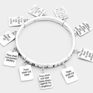 May include: A silver charm bracelet with ten charms, each featuring a different commandment from the Ten Commandments. The charms are square and have black text on a silver background.