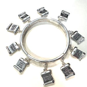 May include: Silver-toned bracelet featuring ten scroll charms, each inscribed with a commandment. The charms are suspended from a circular band. The text on the charms includes phrases like "Have no idols" and "Do not kill."