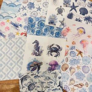 May include: A collection of square paper napkins featuring various nautical and marine life illustrations, including sea turtles, jellyfish, crabs, seahorses, dolphins, whales, seashells, coral, and starfish in shades of blue, pink, and white.