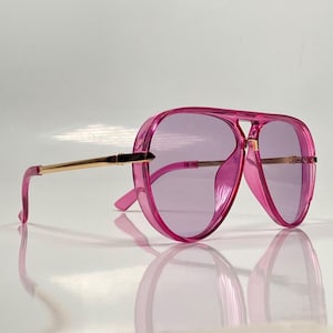 May include: Pink aviator sunglasses with gold metal arms and purple tinted lenses.