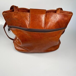 May include: A brown leather tote bag with a zipper closure and two handles. The bag has a flap closure with a magnetic snap. The leather has a textured appearance.