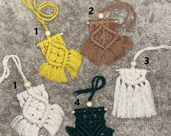 May include: Five macrame wall hangings with wooden beads and fringe. The hangings are in various colors, including yellow, brown, white, and green.