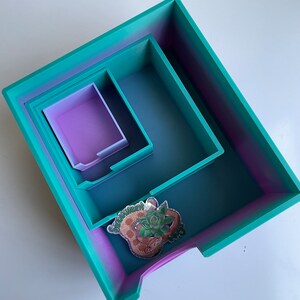 Op de afbeelding: Een set van drie in elkaar passende trays in een verloop van turquoise en paars. De grootste tray heeft een sticker aan de voorkant met de tekst "Succulent Queen".