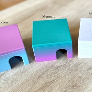Op de afbeelding: Drie kleine, kleurrijke, plastic huisjes met een verloopdesign. De huisjes zijn gelabeld met "E&eacute;nhoorn", "Zeemeermin" en "Marmer Wit".