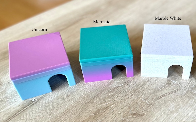 Op de afbeelding: Drie kleine, kleurrijke, plastic huisjes met een verloopdesign. De huisjes zijn gelabeld met "E&eacute;nhoorn", "Zeemeermin" en "Marmer Wit".