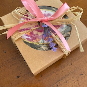 May include: A round, floral patterned coaster with a gold rim, wrapped in brown paper and tied with a pink ribbon and lavender sprigs.