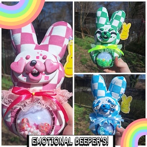 May include: Three decorative bunny figures in pink, green, and blue checkered patterns. Each bunny has a clear, round belly filled with colourful beads and candies. The bunnies have expressive faces and are labelled "Emotional Beeper's!"