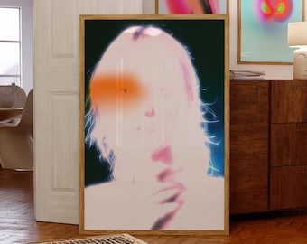 May include: A framed print of a woman's face with a pink and orange glow. The background is dark green and blue. The print is hanging on a wall in a room with wooden floors and a wooden cabinet.