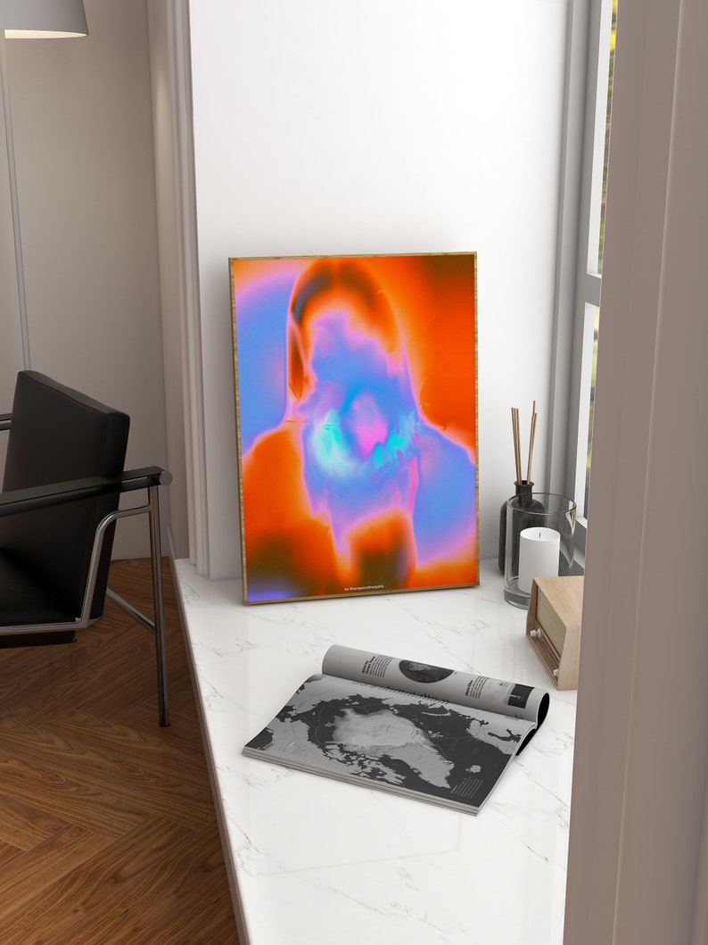 May include: A framed abstract art print with a blurred image of a person's face in shades of orange, blue, and pink. The print is in a gold frame and is hanging on a white wall.