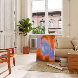 May include: A colorful abstract art print with a blurred image of a person's face. The print is framed in a clear glass frame and is hanging on a wall in a living room.