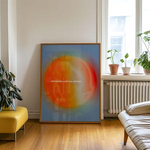 Könnte beinhalten: Ein gerahmter Kunstdruck mit einem abstrakten Design. Ein großer, verschwommener orangefarbener und gelber Kreis vor blauem Hintergrund. Der weiße Text lautet "with intention, with love, with light". Das Kunstwerk wird in einem Raum mit Tageslicht ausgestellt.