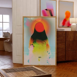 May include: A rectangular wall art print in a light wood frame featuring a central red circle surrounded by a glowing orange halo, transitioning into blended gradients of green, yellow, and blue, with soft, abstract, cloud-like shapes throughout.