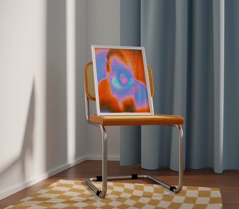 May include: A white framed print of an abstract portrait in shades of orange, blue, and purple, sitting on a wooden chair with a woven back.