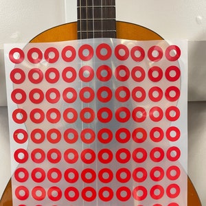 May include: Acoustic guitar with a transparent sheet overlaid, featuring a grid of red circles. The guitar has a natural wood finish, with a dark fretboard and strings. The sheet covers the guitar's body, partially obscuring its details.
