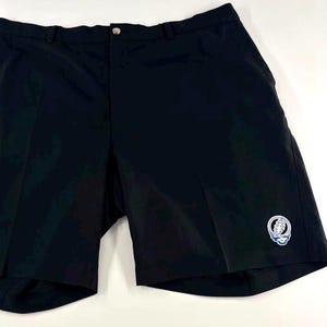 Puede incluir: Pantalones cortos negros con cierre de botón y un pequeño logotipo bordado en la pierna izquierda. Los pantalones cortos parecen estar hechos de un material ligero, adecuado para el clima cálido. El logotipo es azul y blanco.