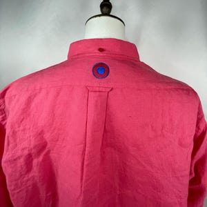 May include: A pink long-sleeved button-down shirt with a red, blue and white circle embroidered on the back.