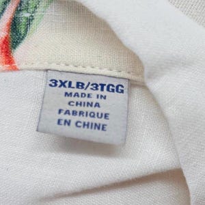 May include: Close-up of a white fabric with a tag. The tag reads "3XLB/3TGG MADE IN CHINA FABRIQUE EN CHINE". The fabric has a floral pattern with red, green, and white colors.