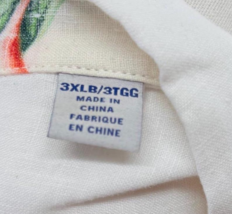 May include: Close-up of a white fabric with a tag. The tag reads "3XLB/3TGG MADE IN CHINA FABRIQUE EN CHINE". The fabric has a floral pattern with red, green, and white colors.