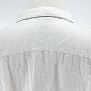 May include: Close-up of the back of a white linen shirt. The collar is visible at the top, with a yoke seam across the shoulders. The fabric has a slightly textured appearance.