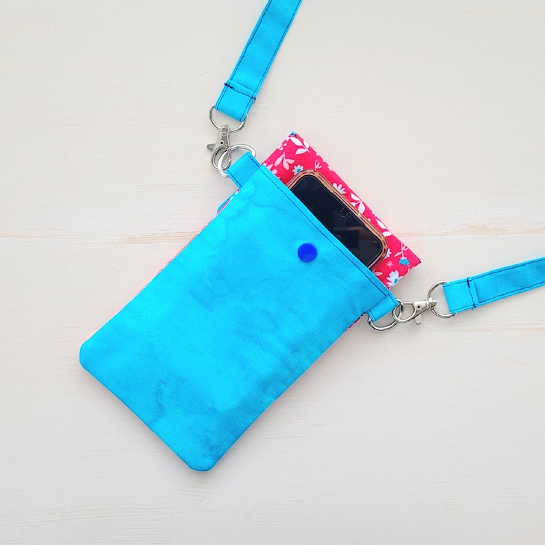 Op de afbeelding: Een felblauwe crossbody telefoonhoes met een binnenzak met bloemenprint en een zilveren sluiting. De hoes is gemaakt van een zachte, textuurrijke stof.