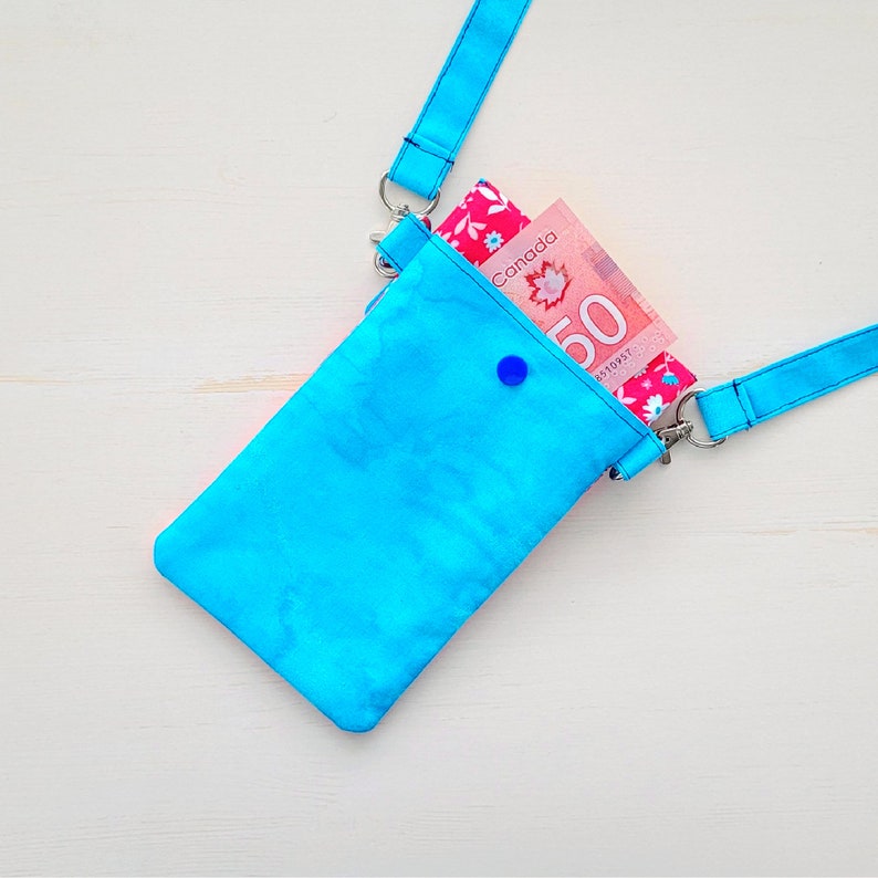 Op de afbeelding: Een felblauwe schoudertas met een voering van roze en witte bloemenprint. De tas is open en er is een Canadees biljet van $ 50 zichtbaar.