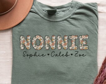 May include: Sage green t-shirt with the word "NONNIE" in floral print letters. Below the word is the text "Sophie ♥ Caleb ♥ Zoe".