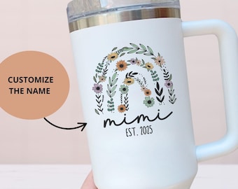 May include: White insulated tumbler with a handle, featuring a floral rainbow design and the name "mimi" with "EST. 2025". The tumbler has a clear lid and a straw. The text "CUSTOMIZE THE NAME" is also visible.