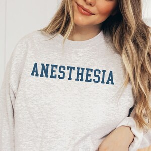 May include: A gray sweatshirt with the word "ANESTHESIA" printed in blue on the front.