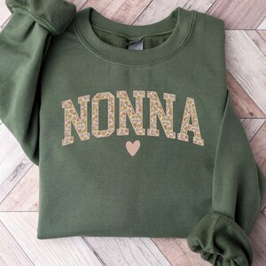 May include: A green sweatshirt with the word "NONNA" printed in floral patterned letters with a small pink heart below.